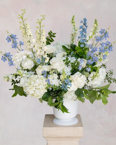 Floral arrangement with white and blue flowers in a vase on a pedestal against a light background