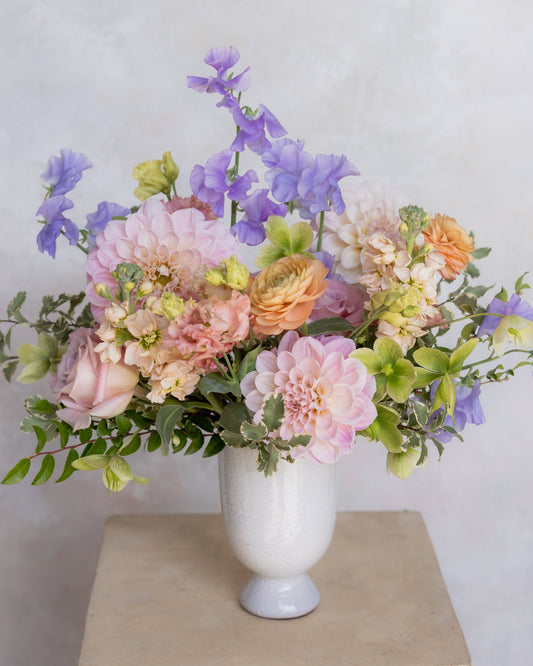 Bouquet of flowers in a white vase on a light surface with a light gray background