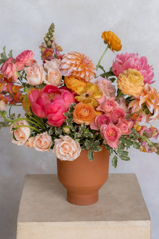 Colorful flower arrangement in a terracotta vase on a neutral background
