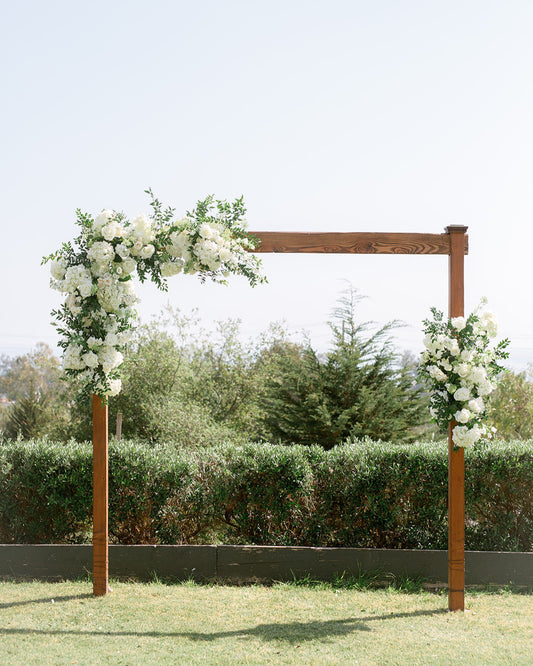Decorative wooden arch with white flowers against a clear sky