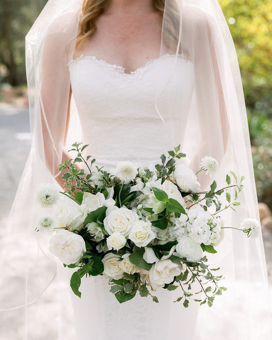 Bride holding a bouquet of white flowers with a blurred natural background