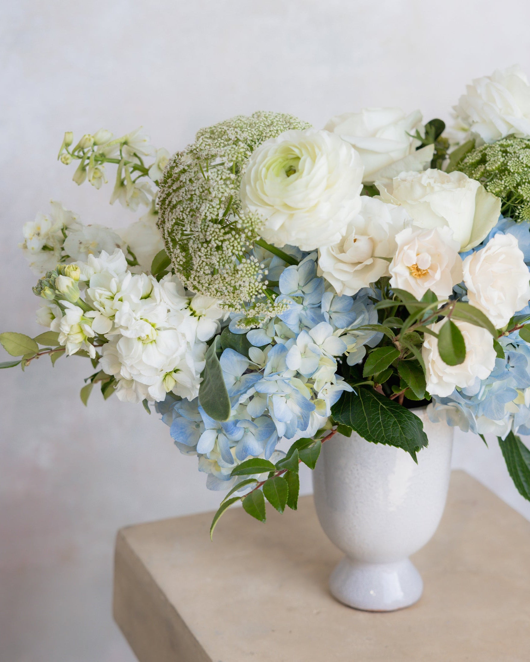 Floral arrangement with white and blue flowers in a white vase on a light surface.