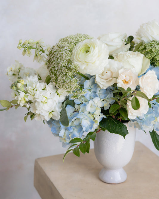 Floral arrangement with white and blue flowers in a white vase on a light surface.